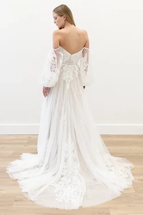 Woman in off-the-shoulder wedding dress, long train, sleeves, and delicate lace detailing.