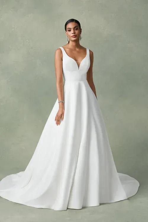 Woman in a white wedding gown with a deep V-neck and a flowing skirt, posing for a photo.