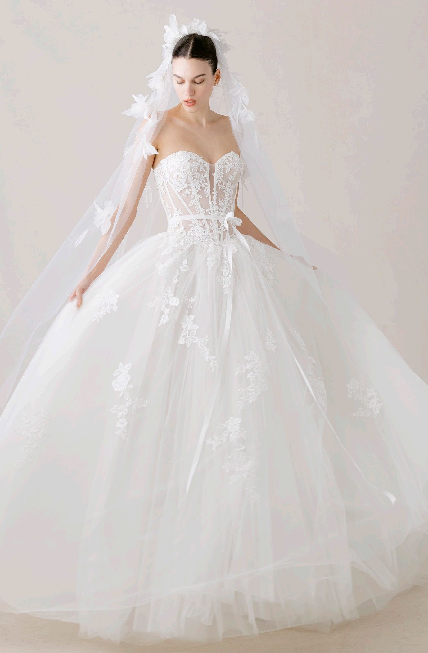 Woman in a white dress with a tulle collar, arms raised, wearing earrings, looking left.