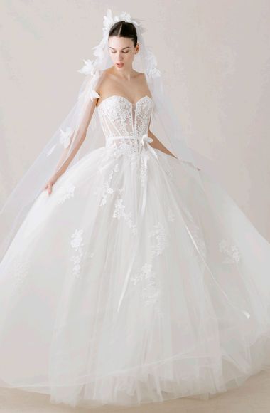 Woman in a white dress with a tulle collar, arms raised, wearing earrings, looking left.