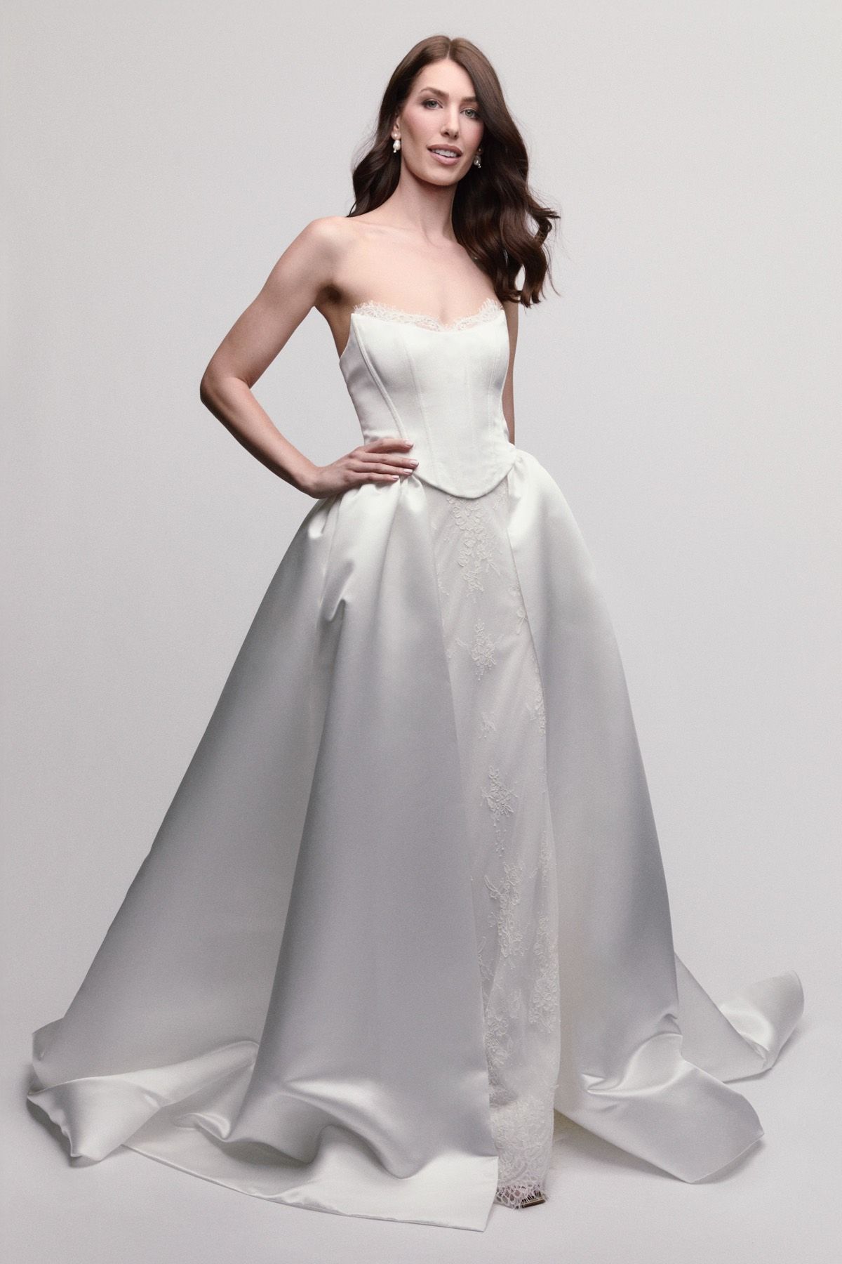 Woman in strapless white wedding gown with sparkling skirt and flowing train, standing in studio.