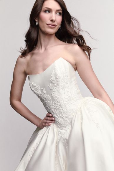 Woman in a white dress with a tulle collar, arms raised, wearing earrings, looking left.