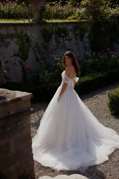 Woman in a white off-the-shoulder wedding dress, posing in a garden.