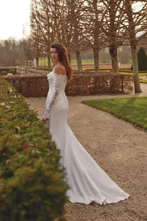 Woman in wedding dress with a train, outdoors, looking over her shoulder.