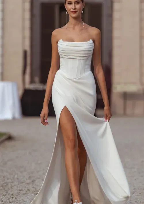 Woman in white strapless dress with high slit, walking outdoors.