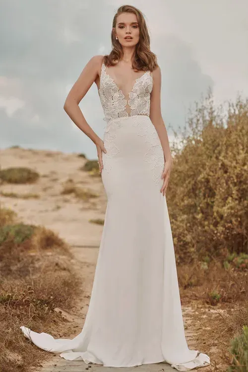 Woman in white wedding dress, deep V-neck bodice with detailed beading, standing outdoors.