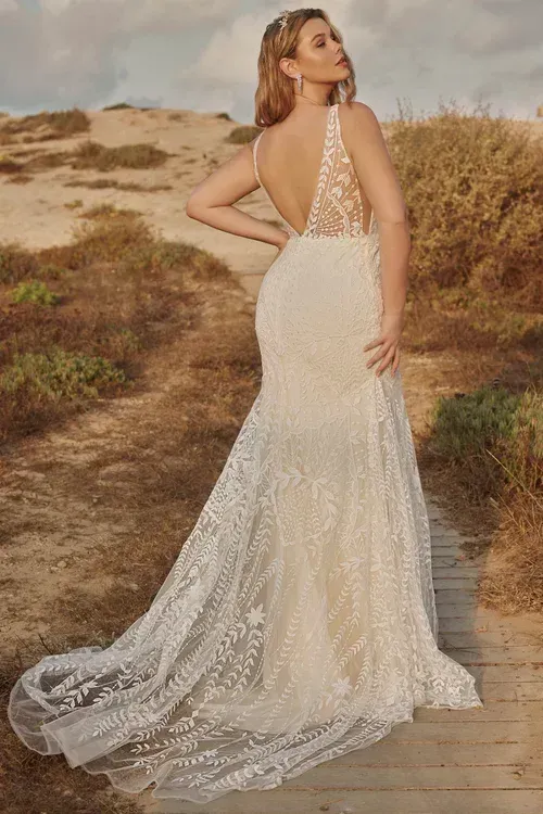 Woman in a white wedding dress with a low back, posing outdoors on a wooden path with a backdrop of dunes.