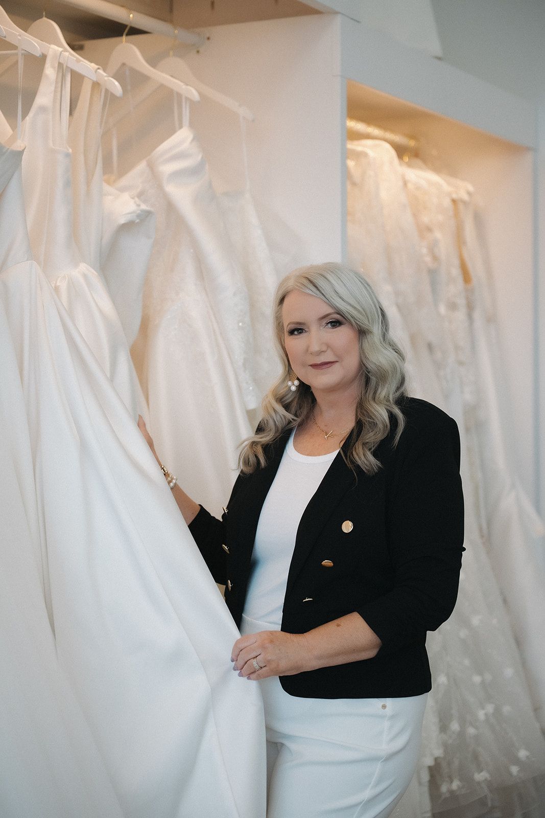 Woman holding a sign with wedding dress shop branding. Blonde hair, smiling, surrounded by dresses.