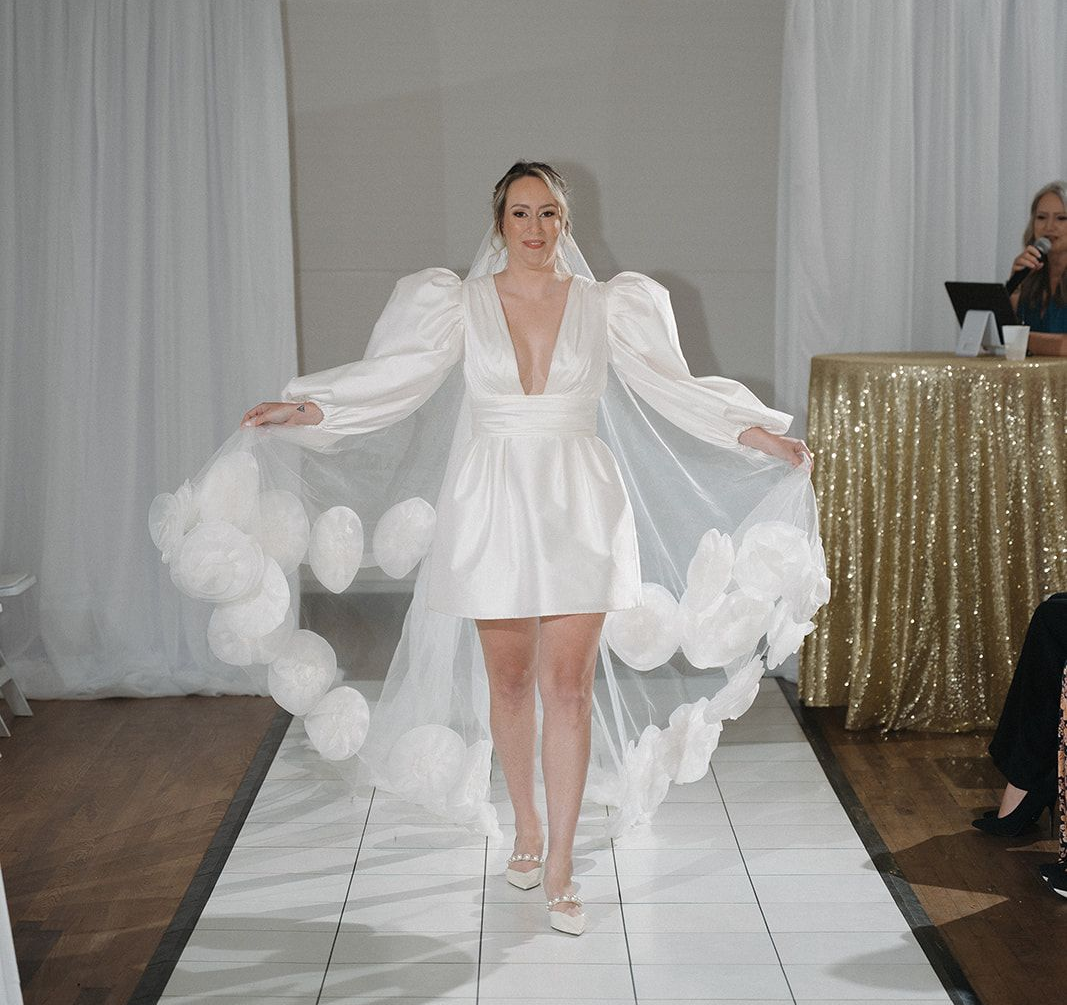 Woman in a white wedding dress with a low back, posing outdoors on a wooden path with a backdrop of dunes.