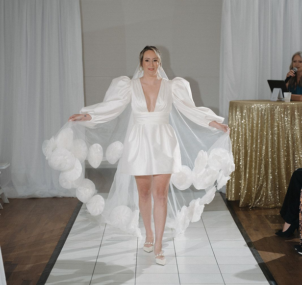 Woman in a white wedding dress with a low back, posing outdoors on a wooden path with a backdrop of dunes.