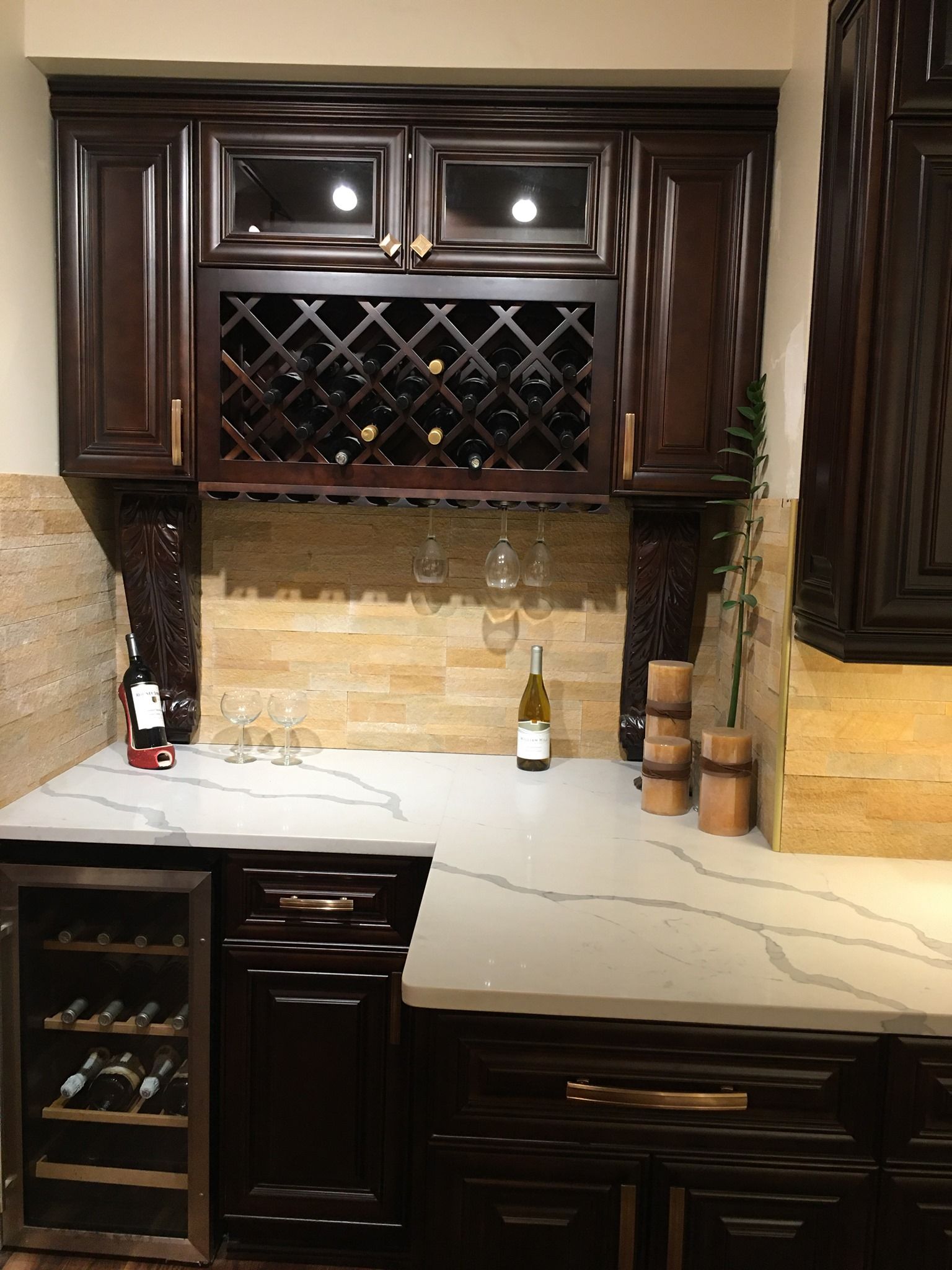 A home wine bar with dark wood cabinetry, a built-in wine rack, white marble-patterned countertops, and a wine fridge.