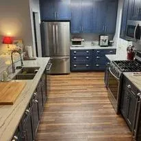 A modern kitchen featuring navy blue cabinets, stainless steel appliances, a wooden floor, and light-colored countertops.
