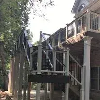 A two-story house exterior featuring a large, multi-level wooden deck with white railings and black balusters.
