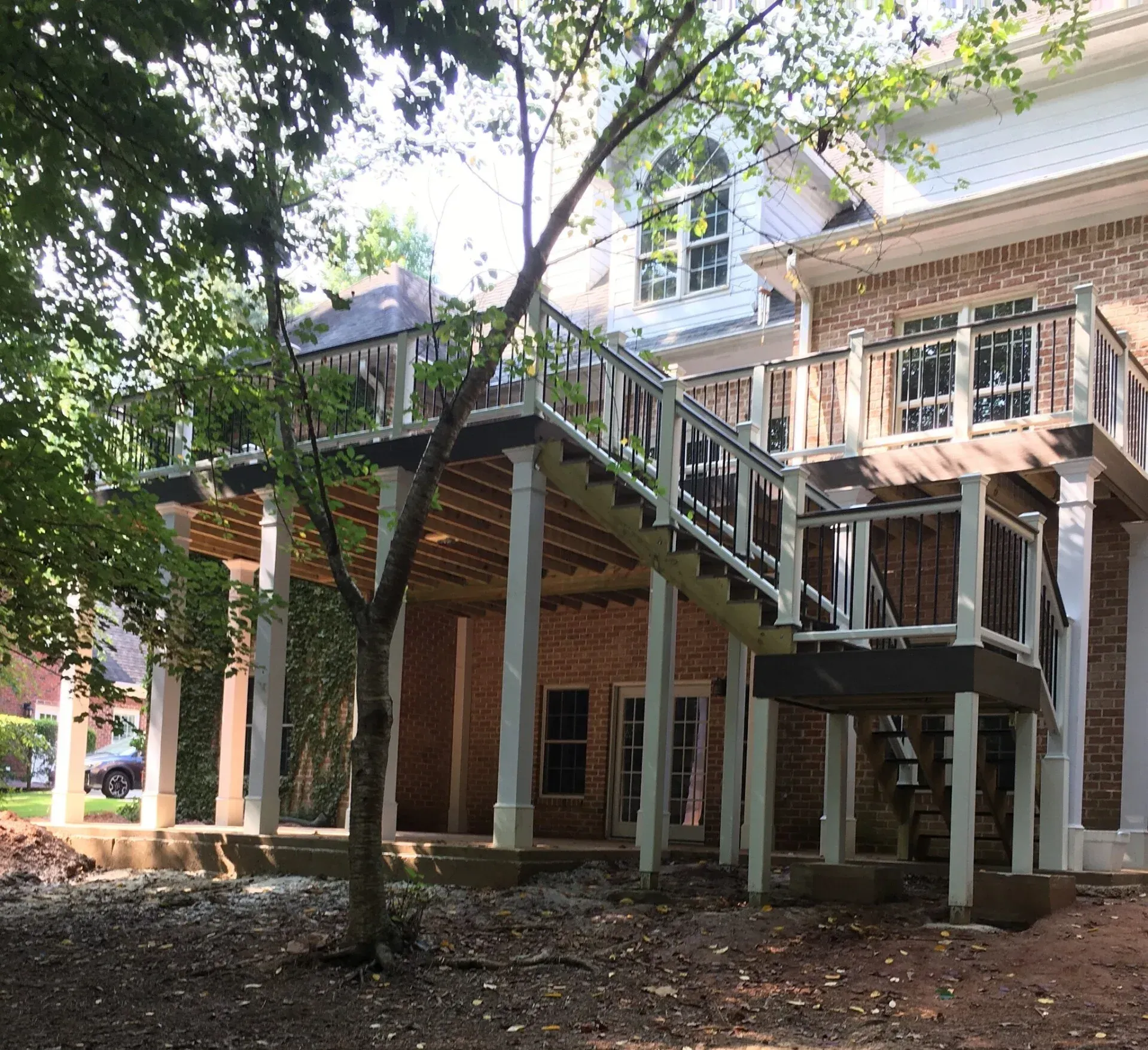 A tall, multi-level wooden deck attached to the back of a brick house, featuring stairs and white support posts.