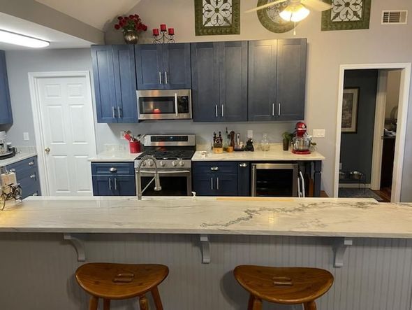 A kitchen with navy blue cabinets, a white marble island, and wooden bar stools under a ceiling fan.