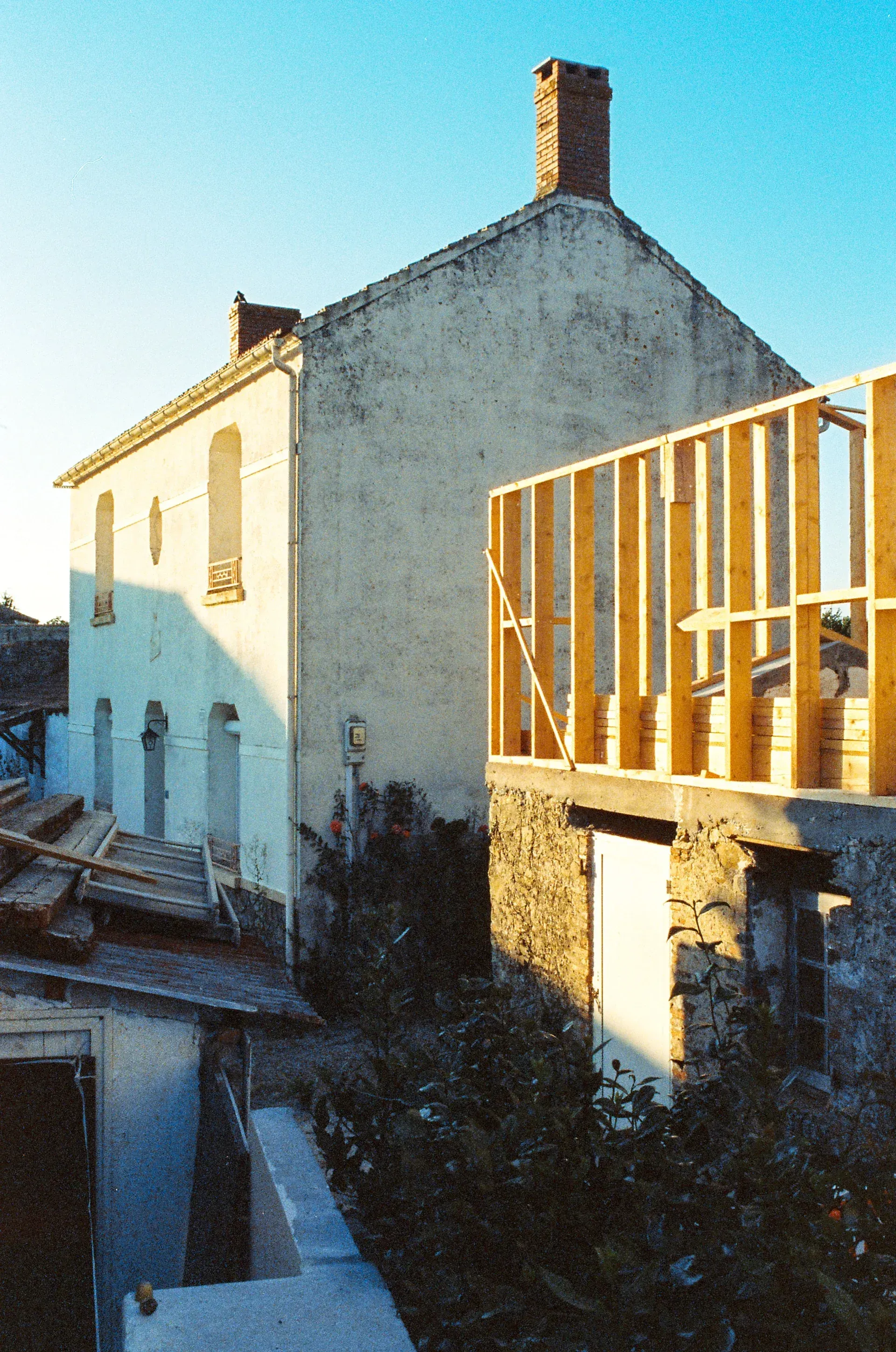 A house under construction with a white plaster wall on the left and an exposed wooden frame structure on the right.