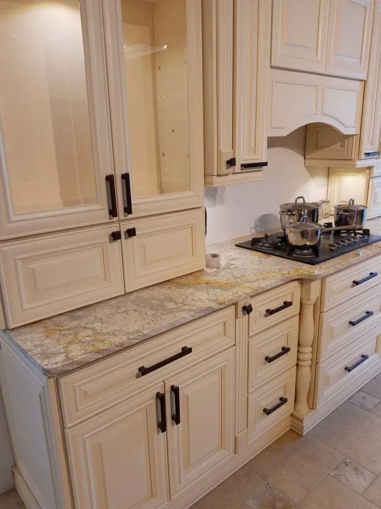Cream-colored kitchen cabinets with dark hardware and granite countertops, featuring a stovetop with pots.