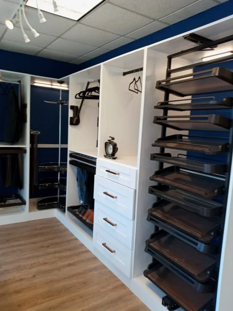 A walk-in closet featuring white cabinets with drawers, dark pull-out shelves, hanging rods, and blue walls.