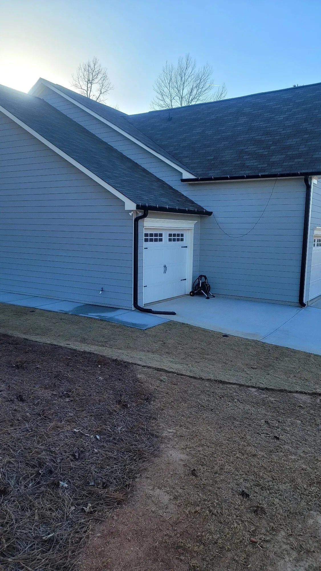 Light blue house exterior with a white door and dark trim, featuring a dark-colored roof under a bright, sunny sky.