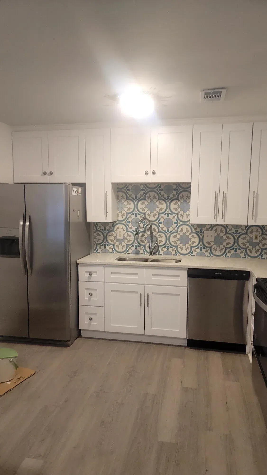 A kitchen featuring white cabinets, stainless steel appliances, and a patterned blue-and-white tile backsplash.