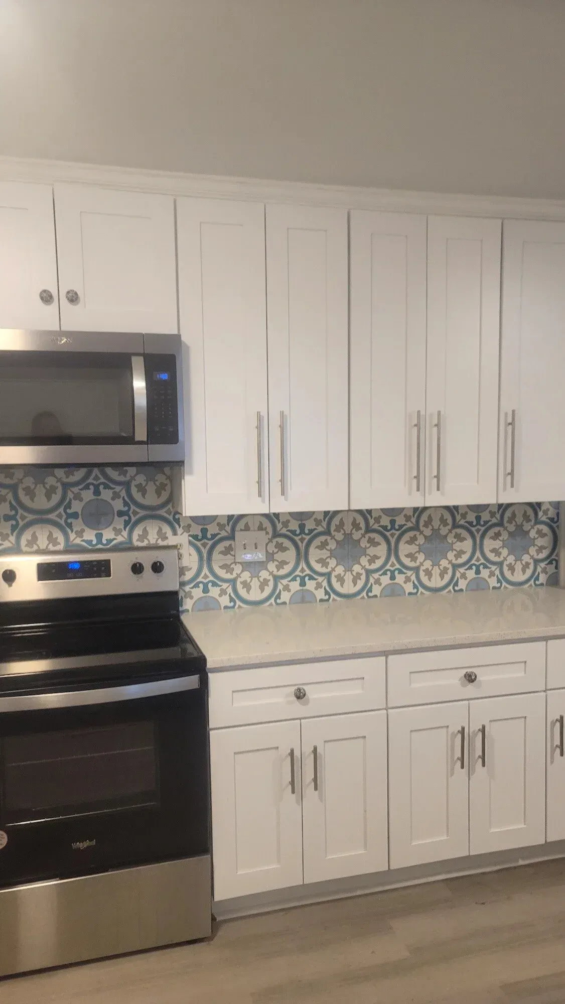 Kitchen featuring white Shaker cabinets, stainless steel appliances, and a decorative blue and white patterned backsplash.