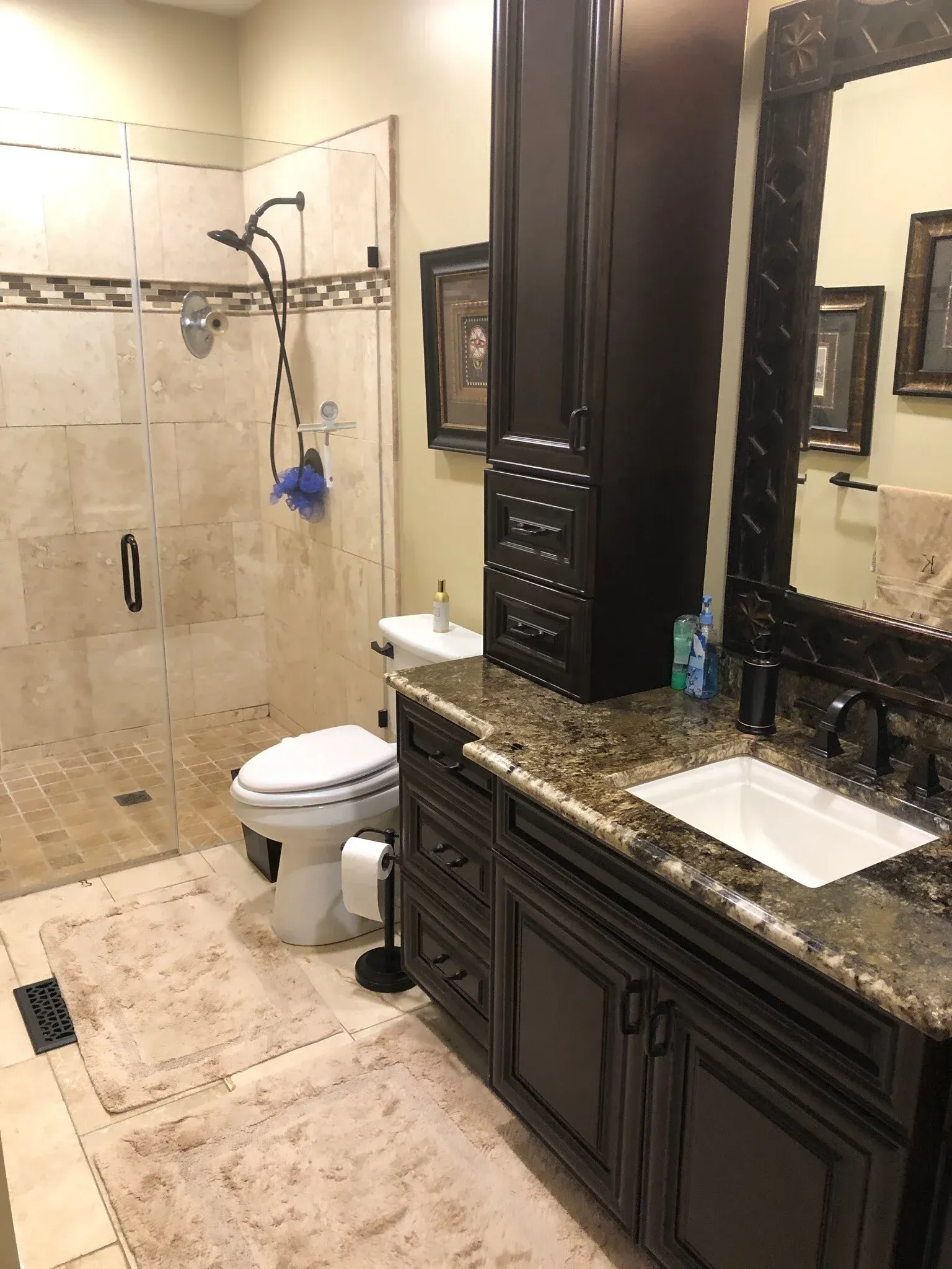 A bathroom featuring a stone walk-in shower, a toilet, and a dark wood vanity with a granite countertop and framed mirror.
