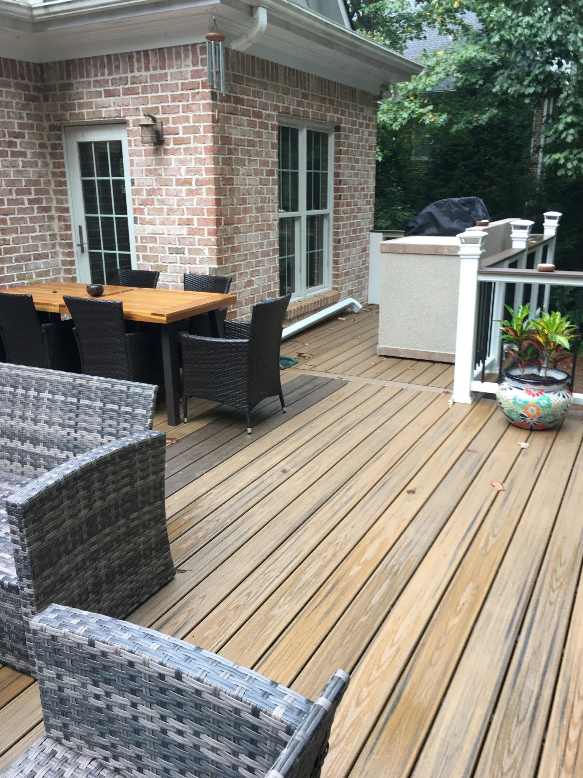 A wooden deck with patio furniture, a dining set, and a potted plant outside a brick house.