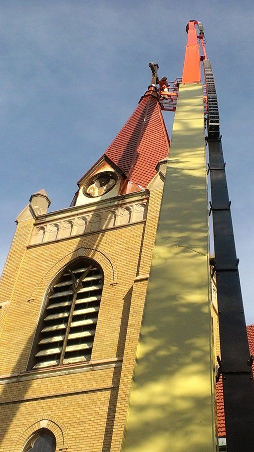 A tall building with a red roof is being painted by a crane.