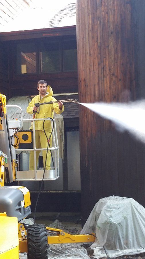 A man is cleaning a wooden building with a high pressure washer.