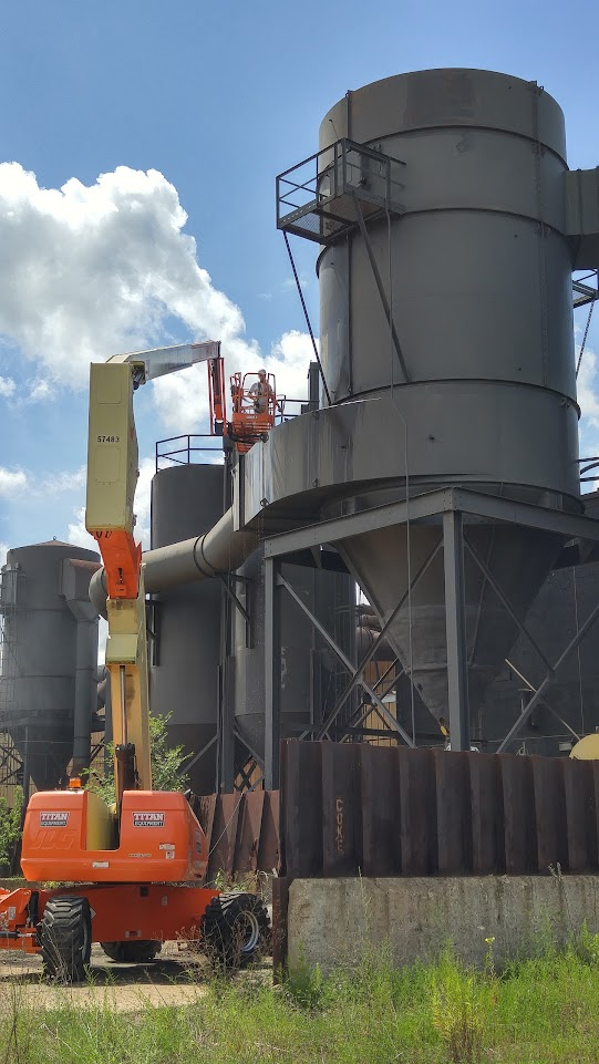 A man is standing on a crane in front of a large building.