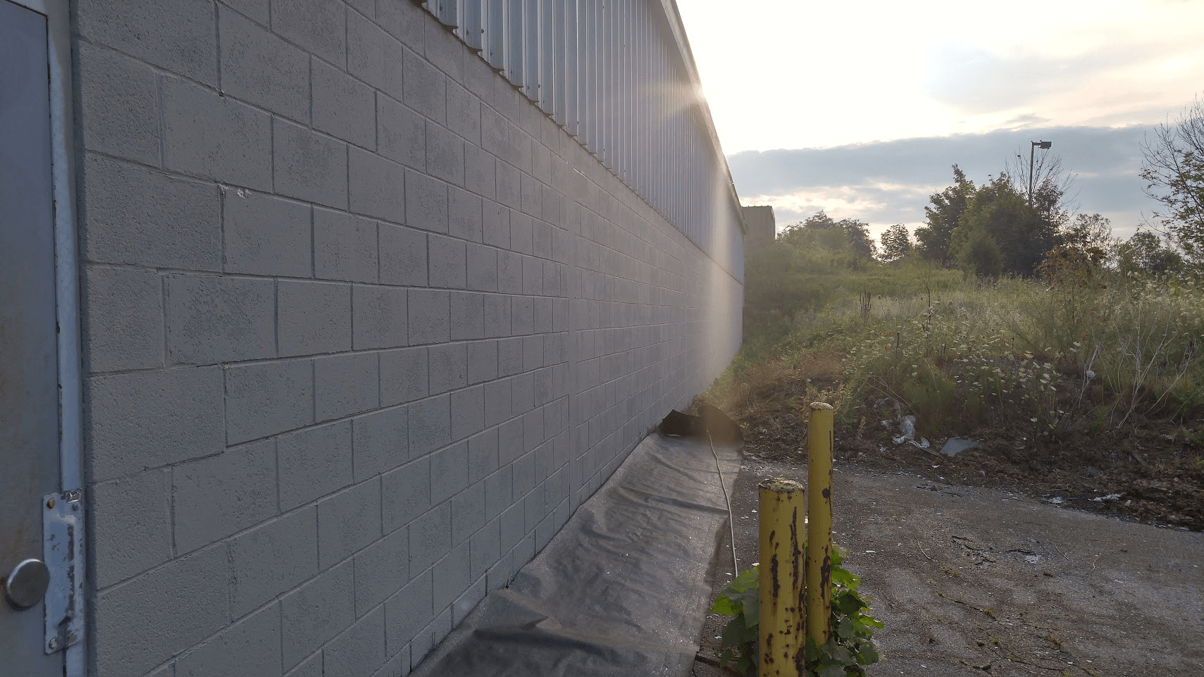 A brick wall with a door and a yellow pole in front of it.