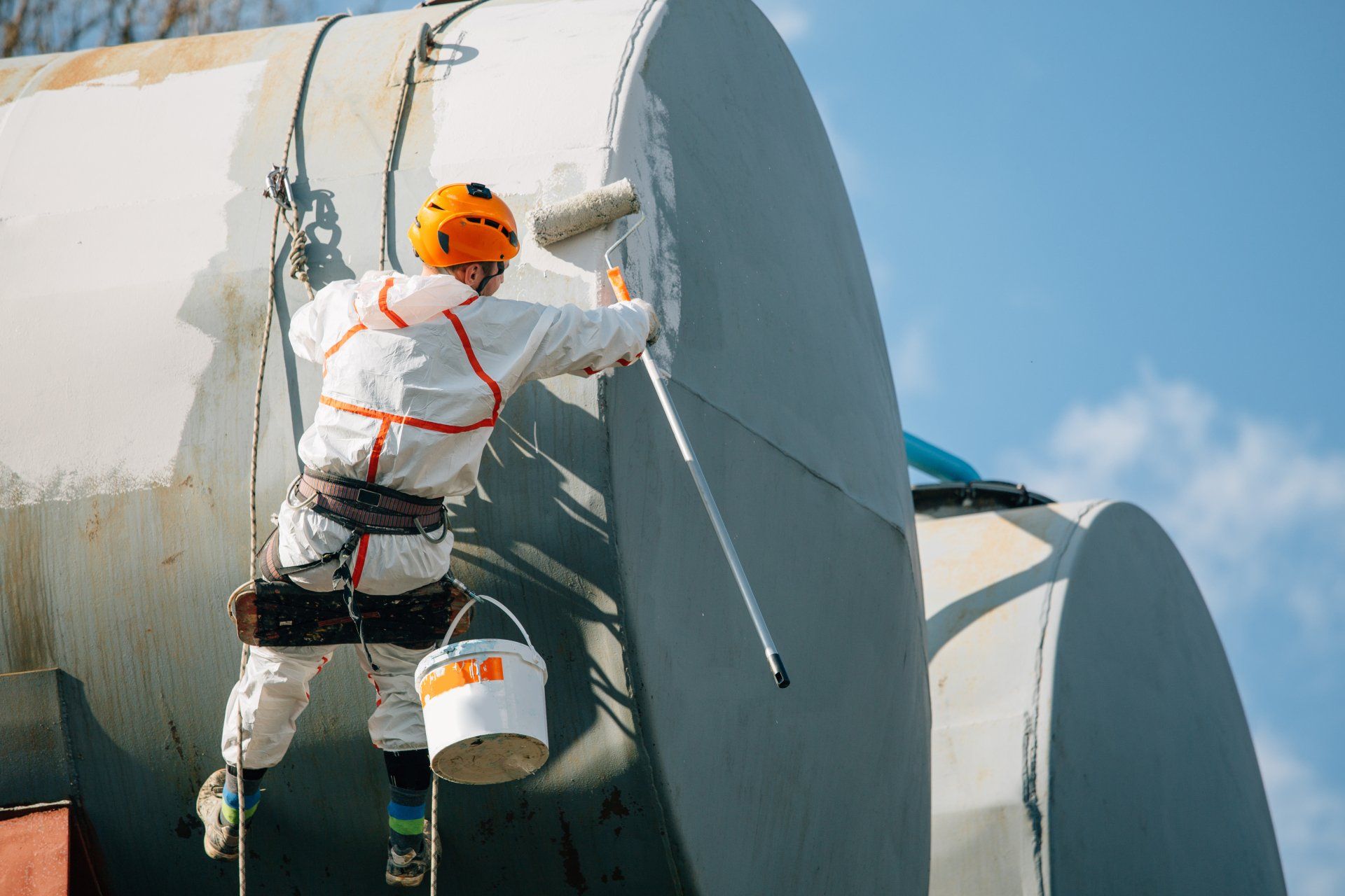 A man is painting a large pipe with a roller.