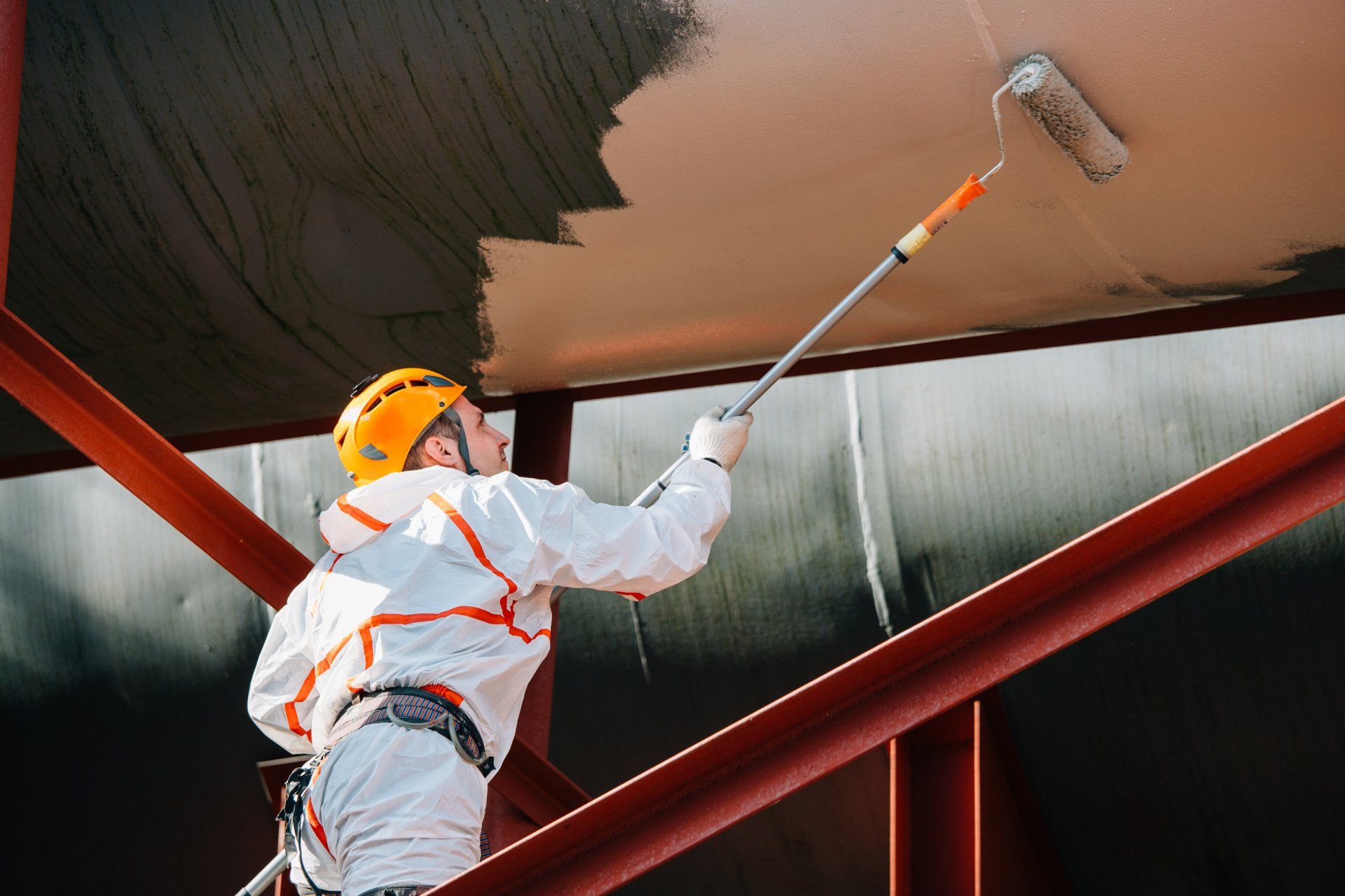 A man is painting a pipe with a roller.