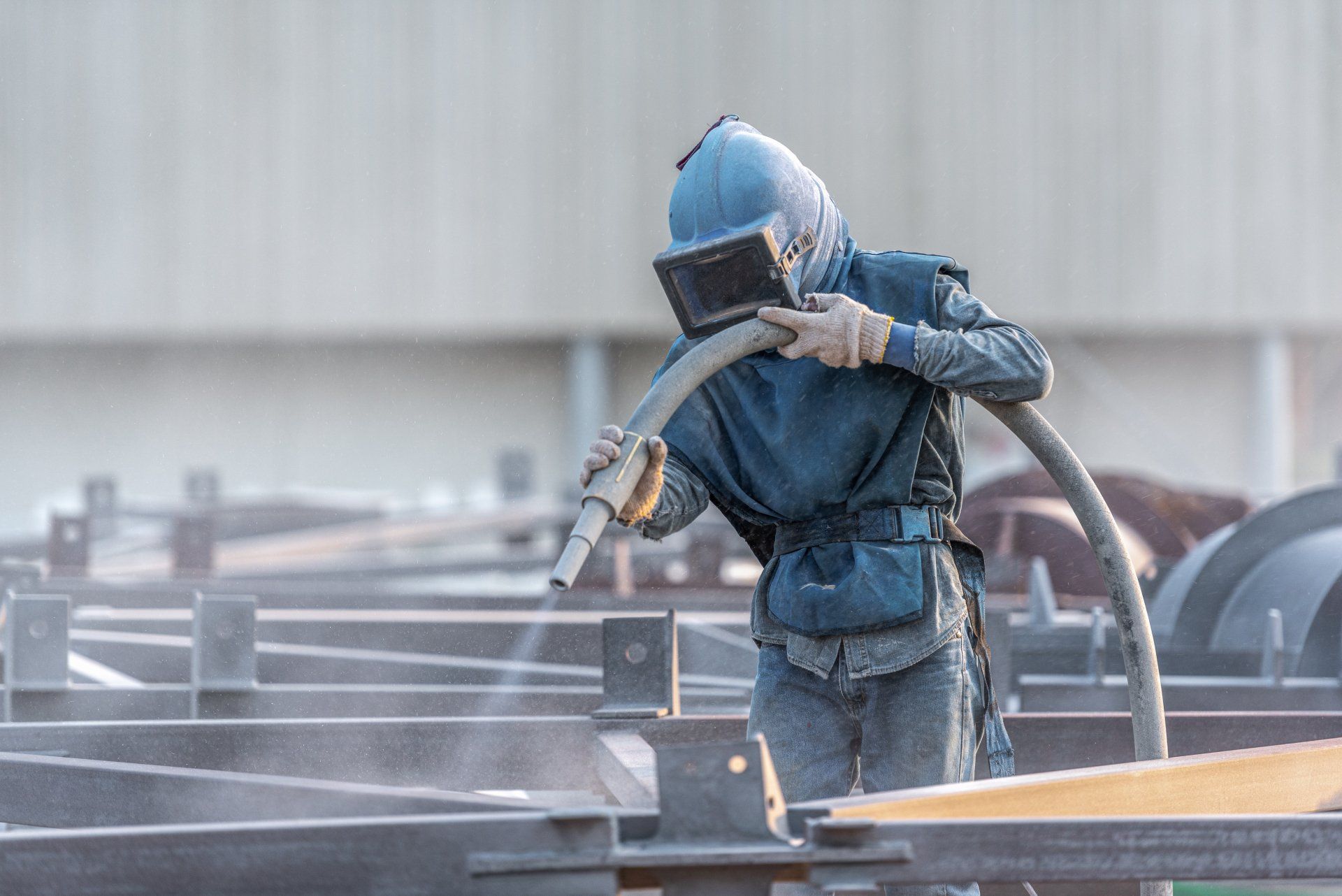 A man is sandblasting a metal structure in a factory.
