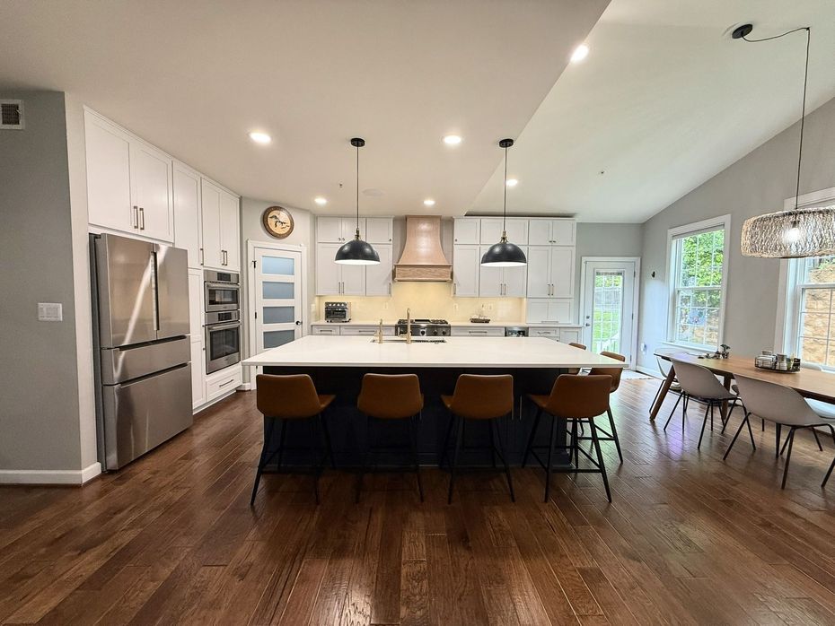 Modern open-plan kitchen and dining area with white cabinets, stainless fridge, dark wood floors, and pendant lights