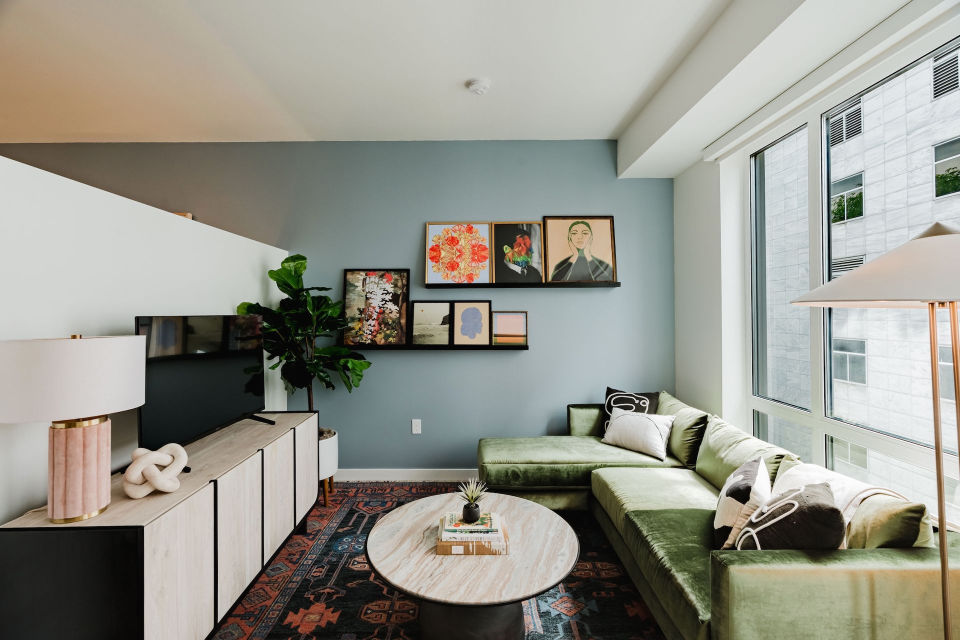 Bright modern living room with green sectional, round coffee table, wall art, and large windows