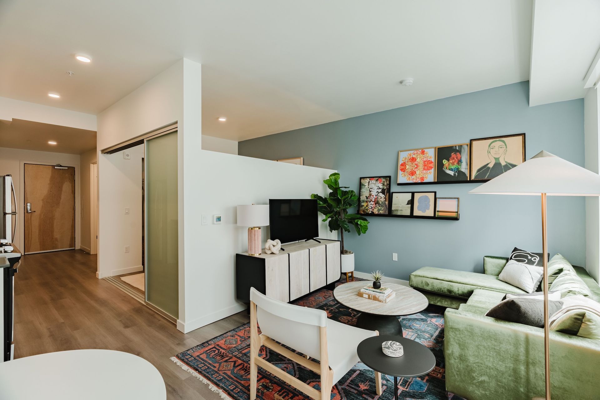 Modern living room with green sofa, TV console, wall art, and hallway in an open apartment.