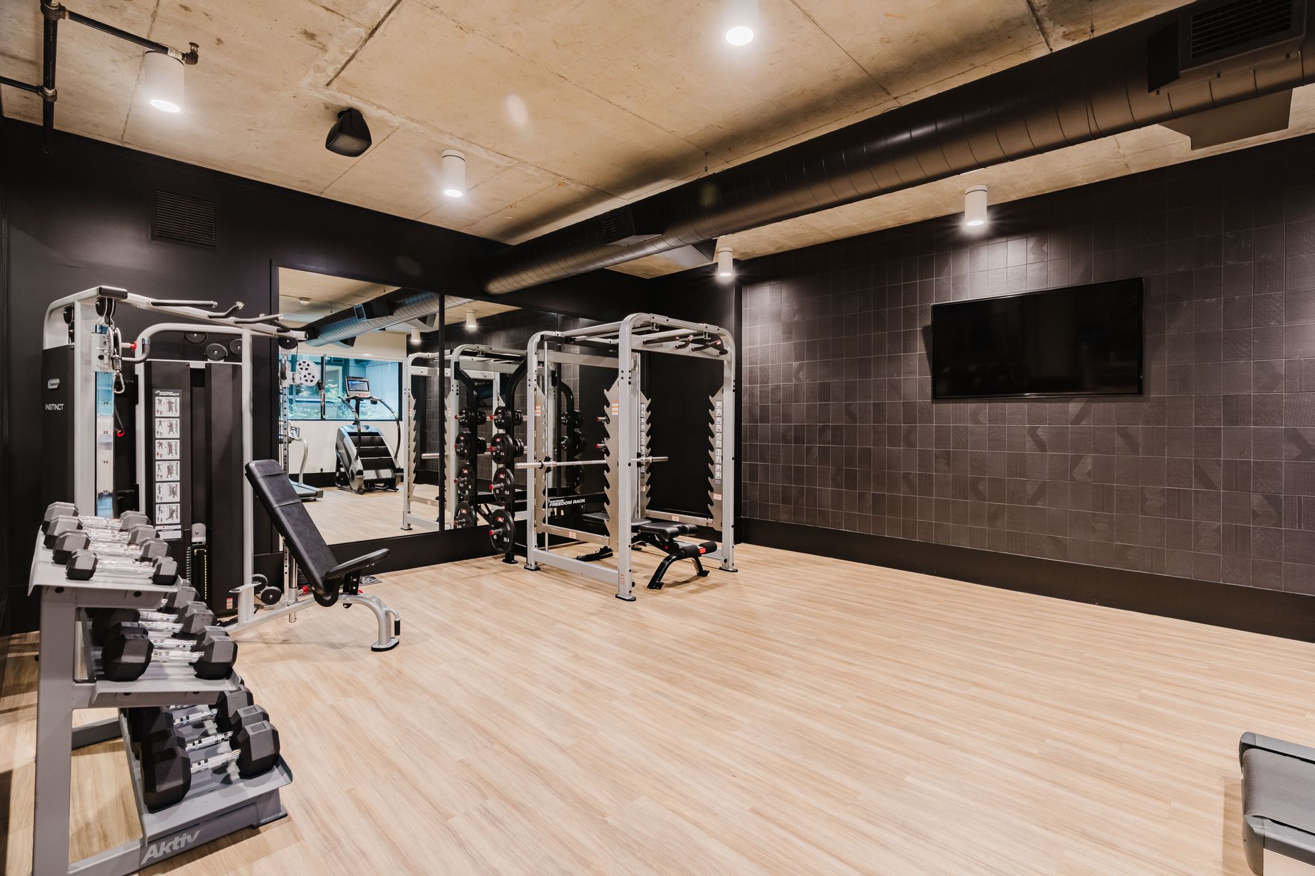 A gym with a lot of equipment and a flat screen tv on the wall.
