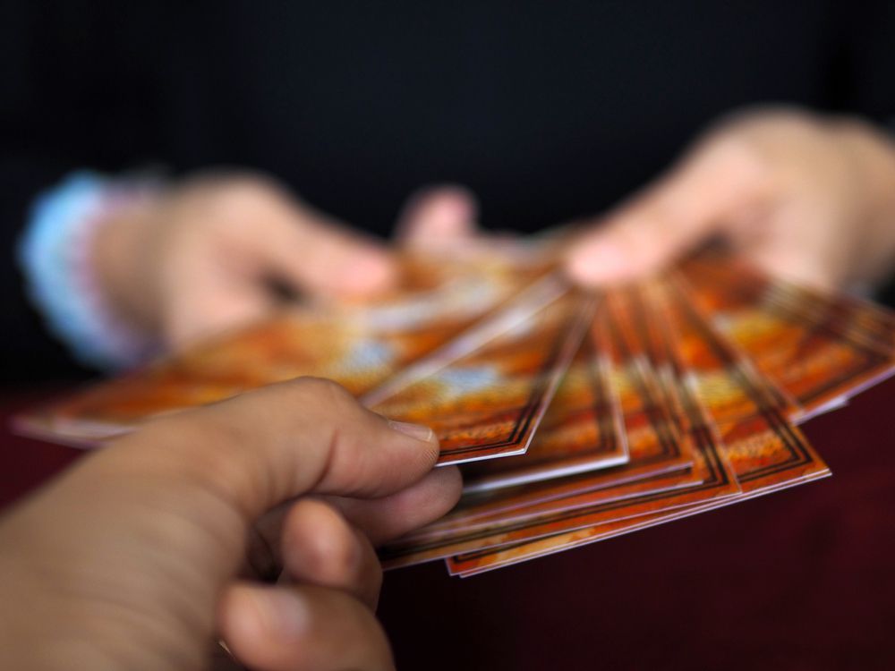 Hand holding a card over a game table with dice and other cards. Purple surface, warm lighting.