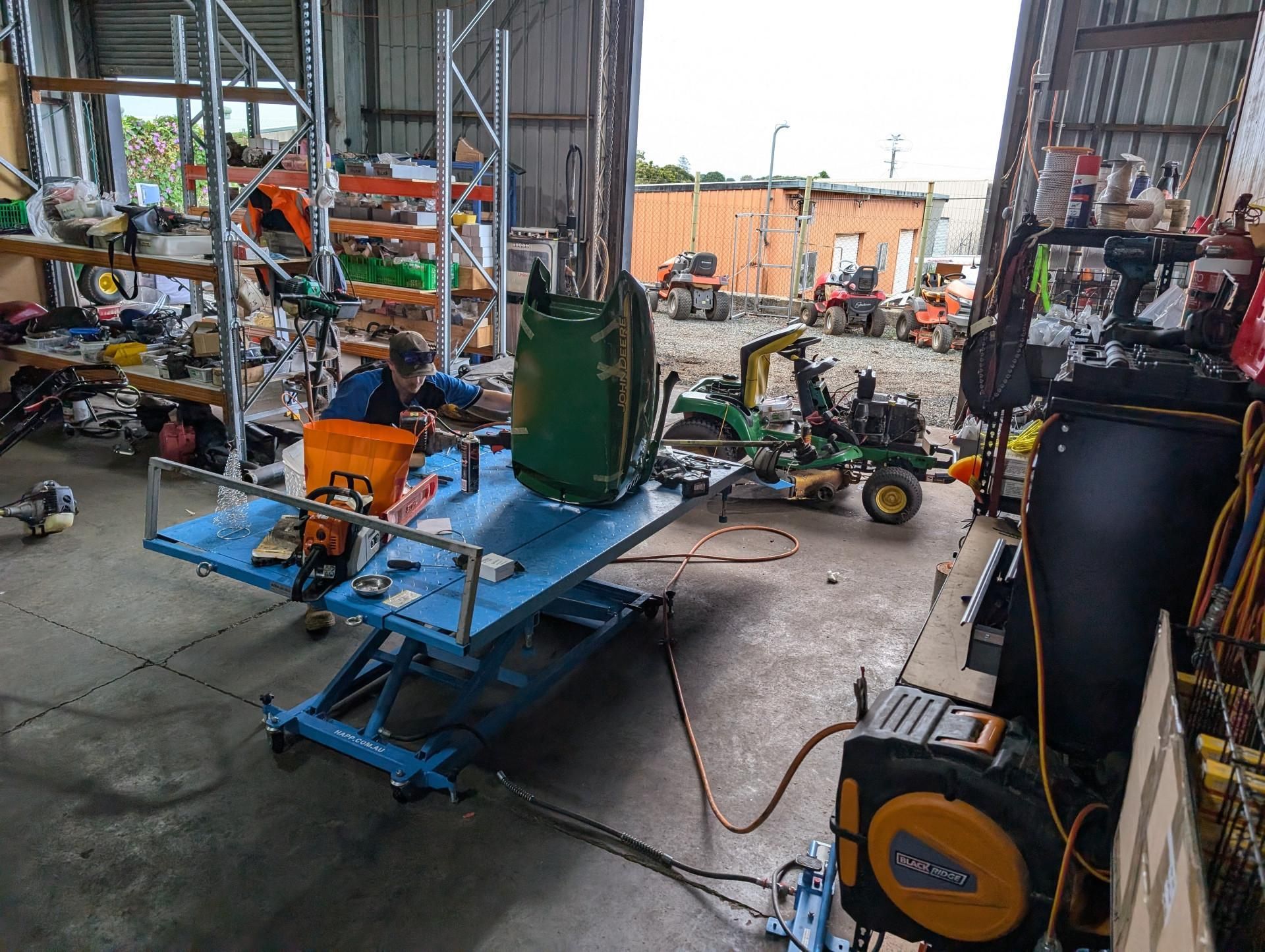 A Man Is Working On A Lawn Mower In A Garage — Plateau Mower Repairs In Ballina, NSW