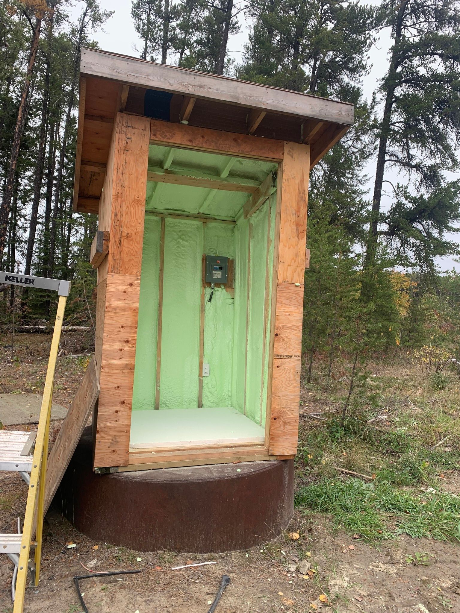 a wooden outhouse is being built in the middle of a forest .