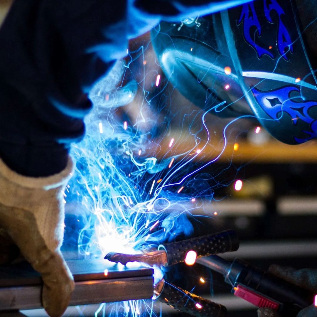 A person wearing a welding helmet is welding a piece of metal