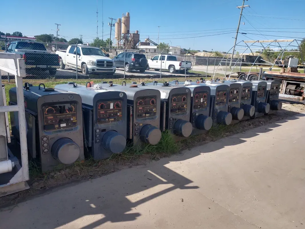 A row of welding machines are lined up in a parking lot.