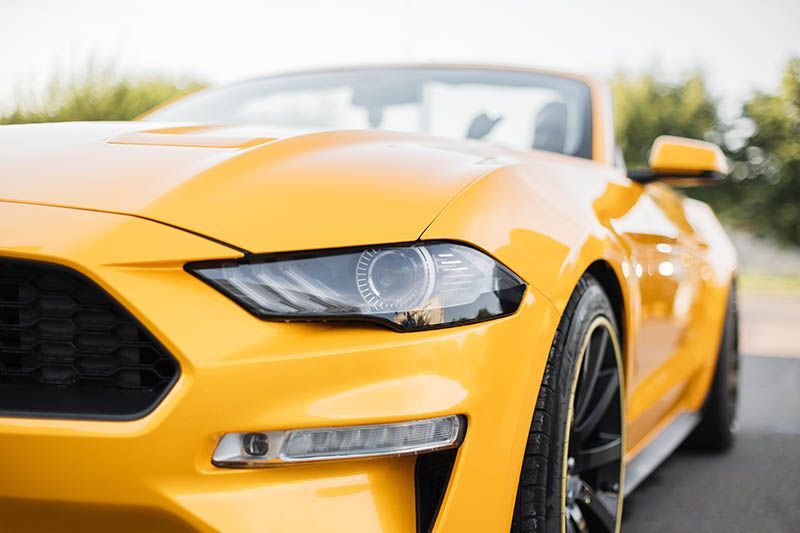 Yellow sports car parked outdoors, front close-up with headlights and grille visible