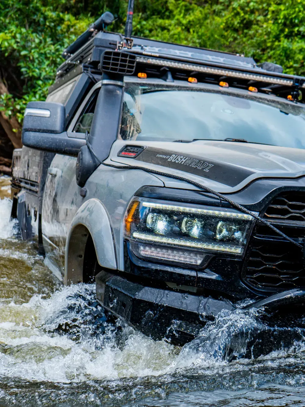 Gray off-road truck splashing through a shallow stream in a wooded trail