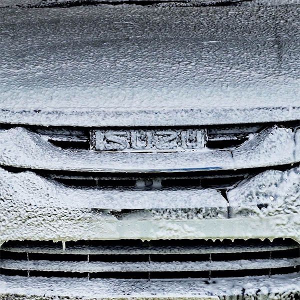 Snow-covered car front grille and license plate with heavy frost on the bumper and hood