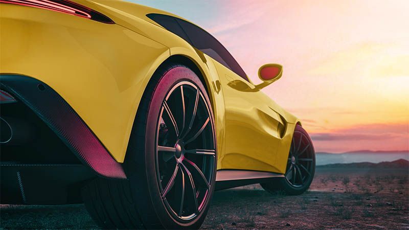 Yellow sports car parked at sunset on a road with mountains in the distance