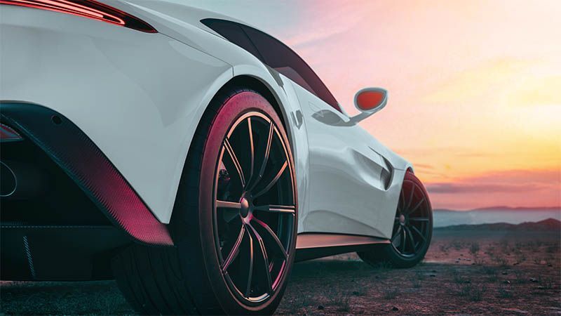 White sports car at sunset on a road, rear view with black rims and pink accents, against a colorful sky