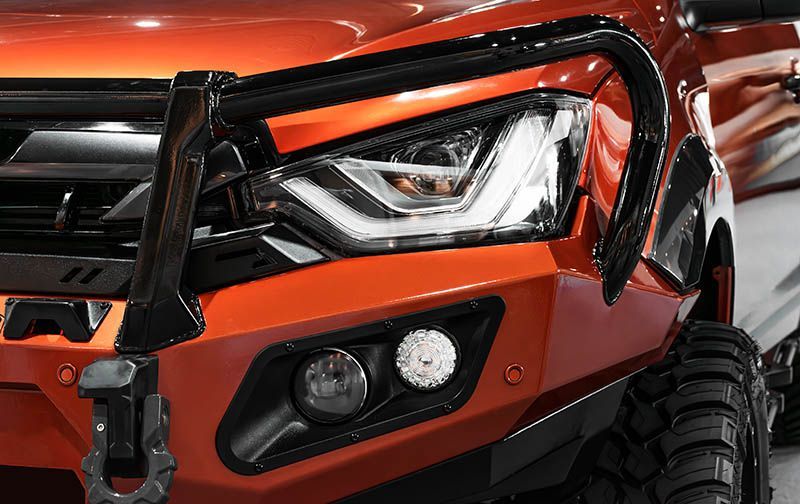 Close-up of an orange off-road vehicle’s front headlight and bumper with a rugged tire