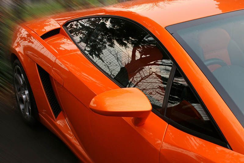 Orange sports car viewed from above, with dark tinted windows and a sleek side mirror